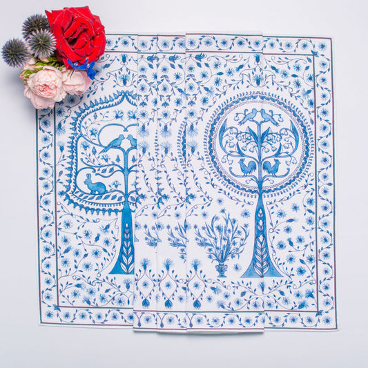 Decorative tablecloth with blue floral and tree pattern on a white background, accompanied by red and pink flowers.