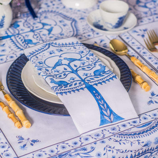Table setting with blue and white patterned tablecloth, plates, napkins, and cutlery.