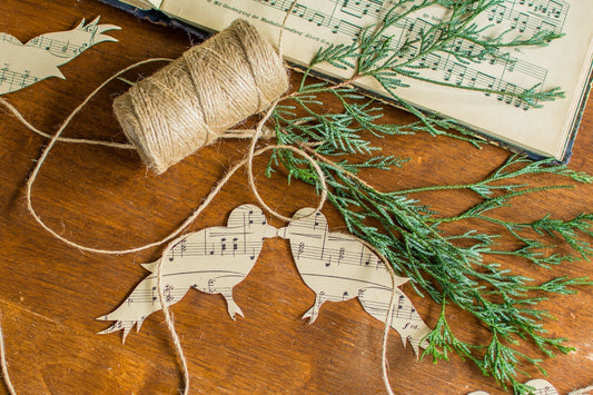 Handmade Christmas garland made from cut-out music-notes, twine, and tape styled on a wooden table with greenery.