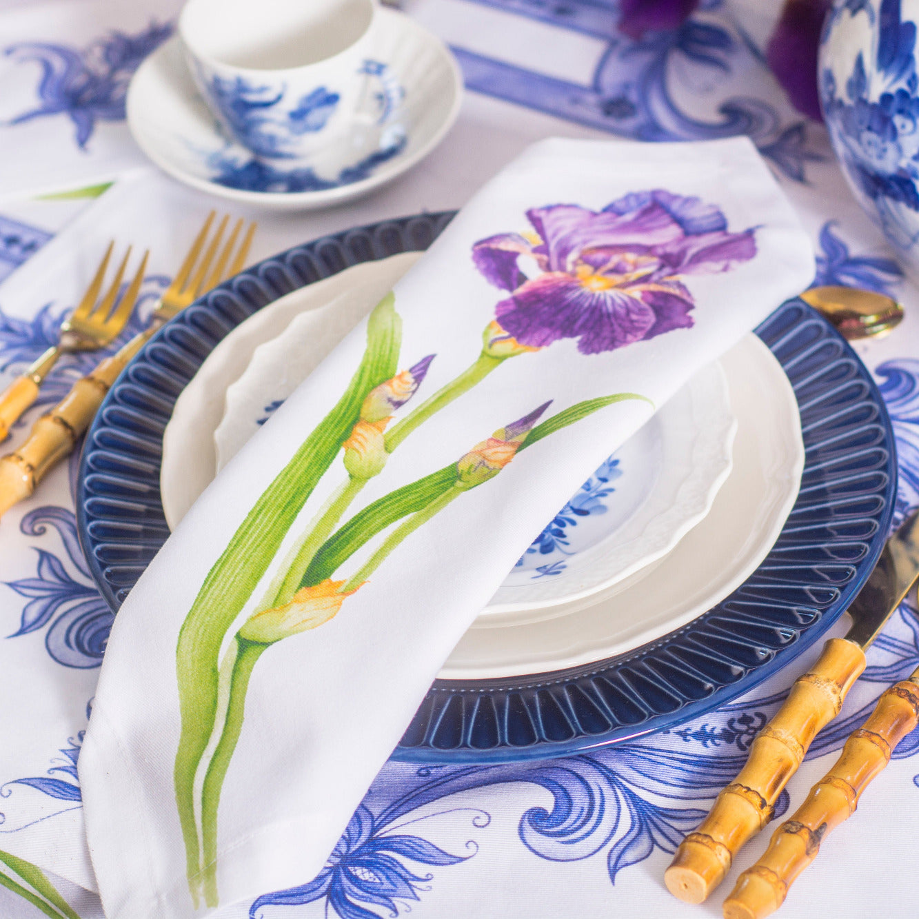 Table setting with blue and white plates, floral napkin, and decorative tablecloth.