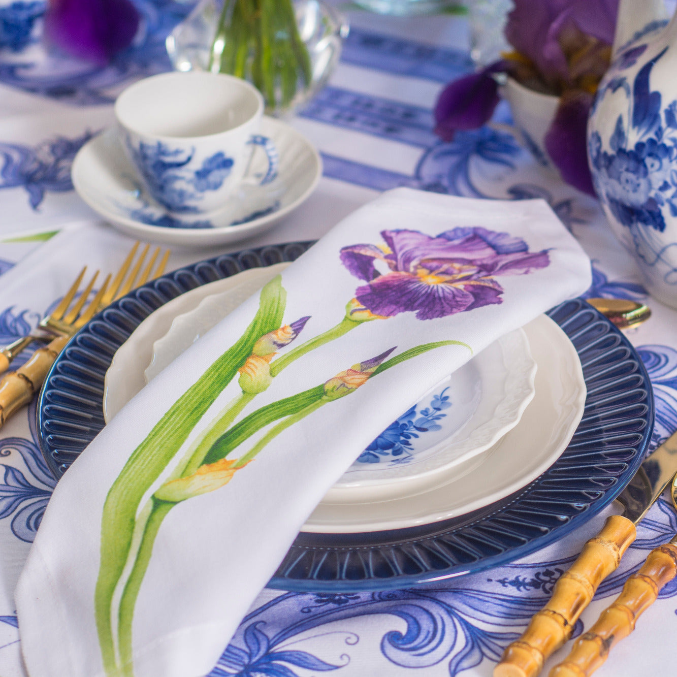 Dining table setting with blue, PURPLE  and white floral patterns on tablecloth, plates, and teapot.