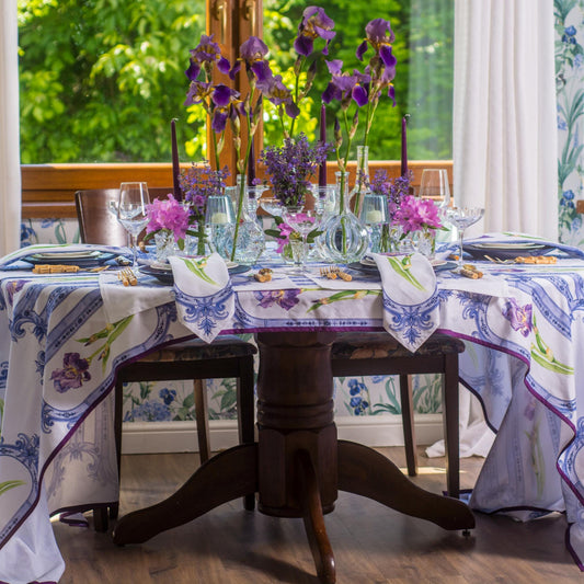 Dining table set with a floral tablecloth and centerpieces in a room with floral wallpaper.