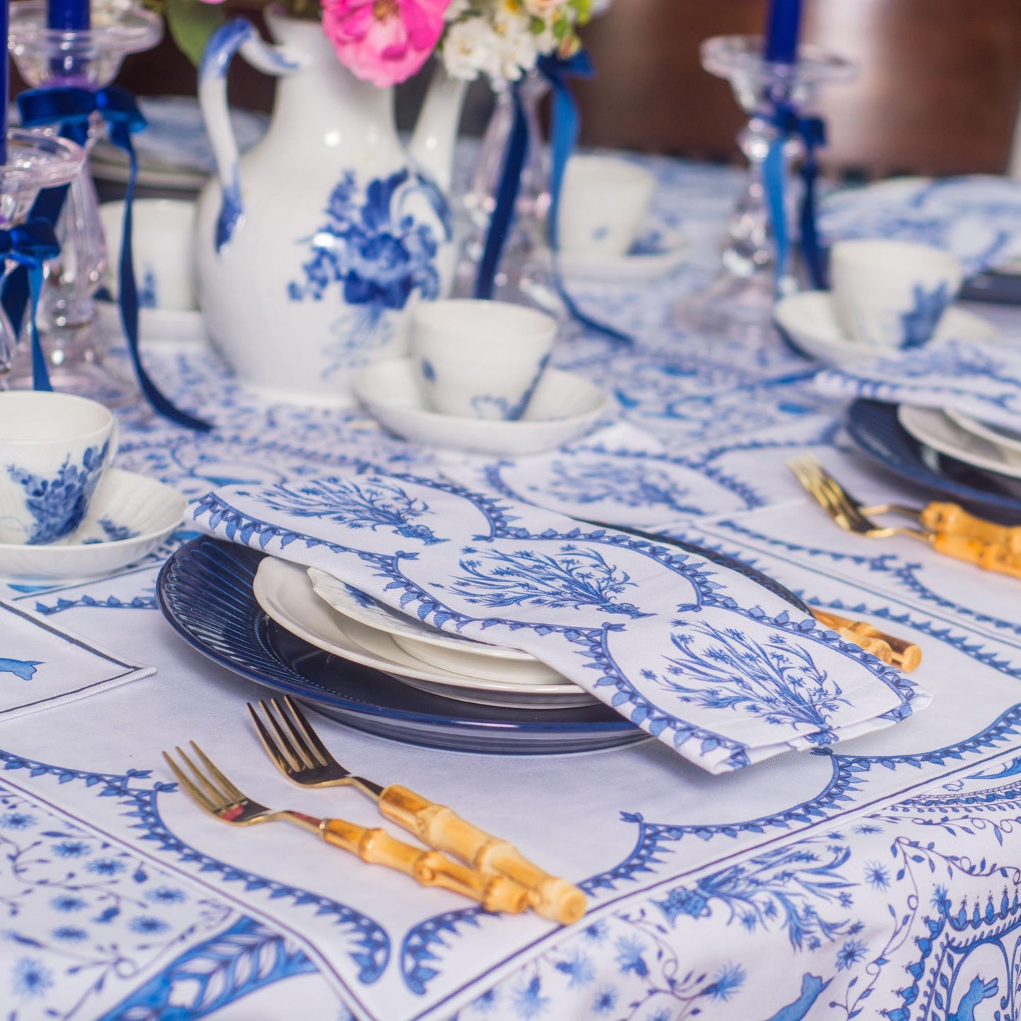 Dining table set with blue and white crockery, cutlery, and napkins on a patterned tablecloth.