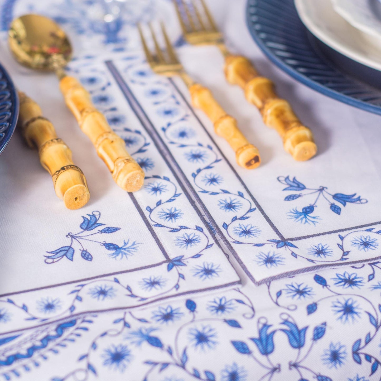Decorative table setting with blue and white patterned placemats, blue plates, and yellow cutlery.