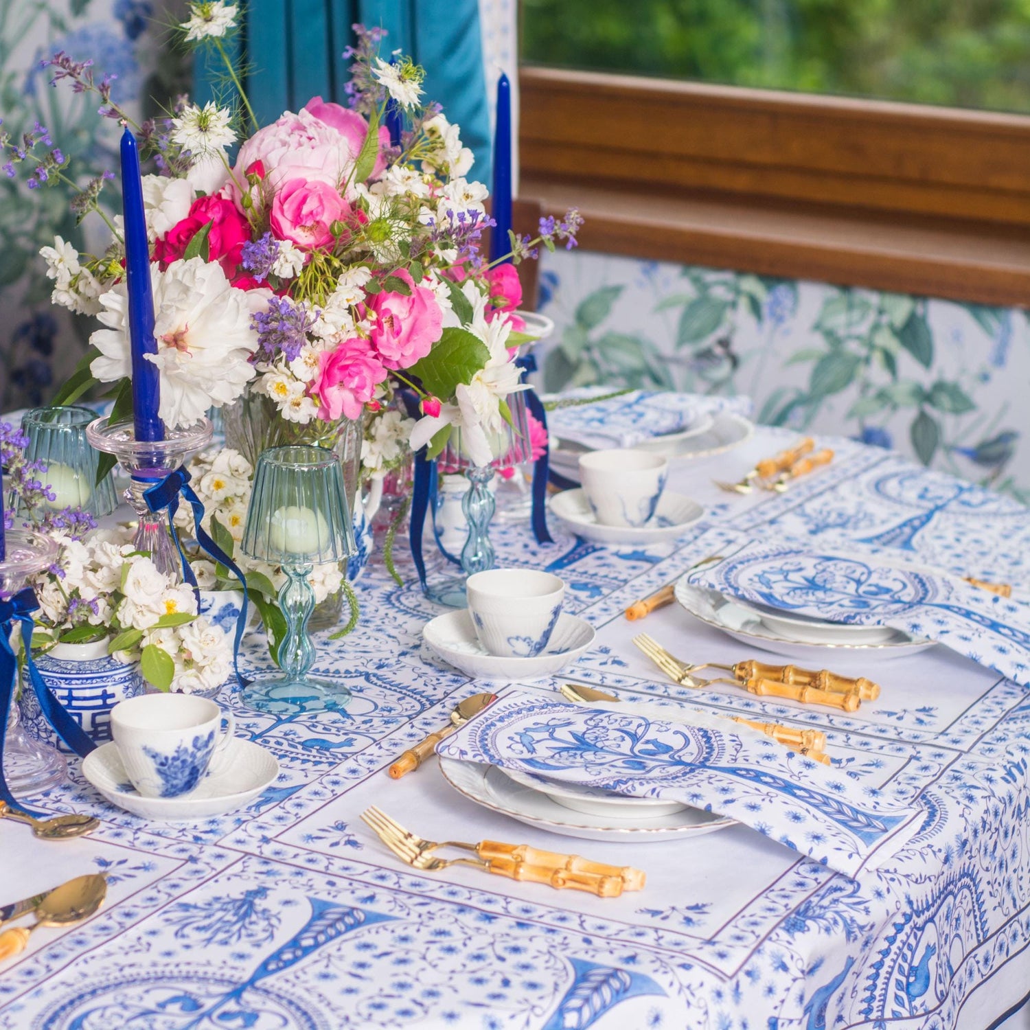 Elegant table setting with blue and white tablecloth, napkins and placemats, floral centerpieces, and blue candles.